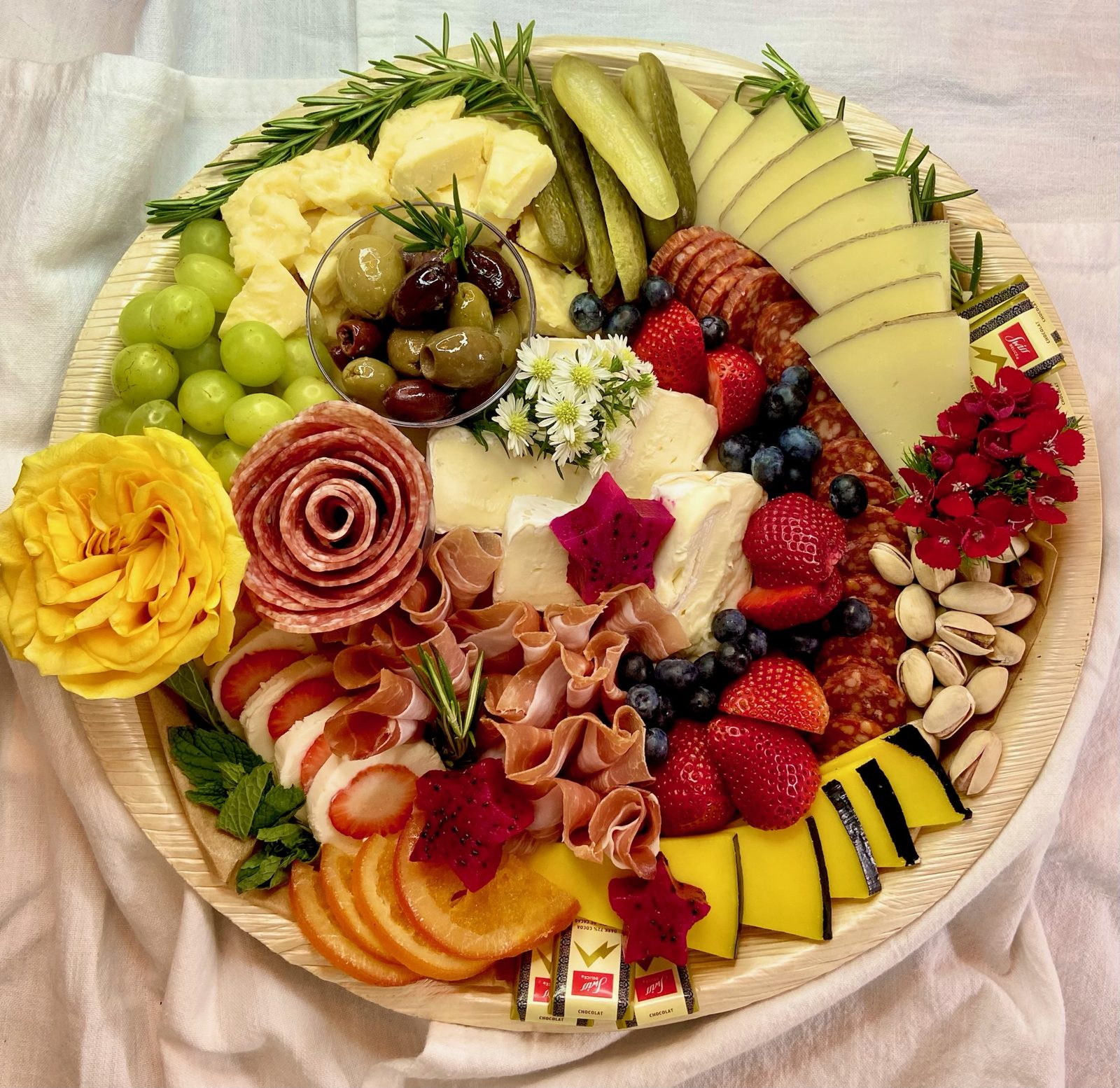 Round charcuterie board with meat roses, cheeses, and yellow roses