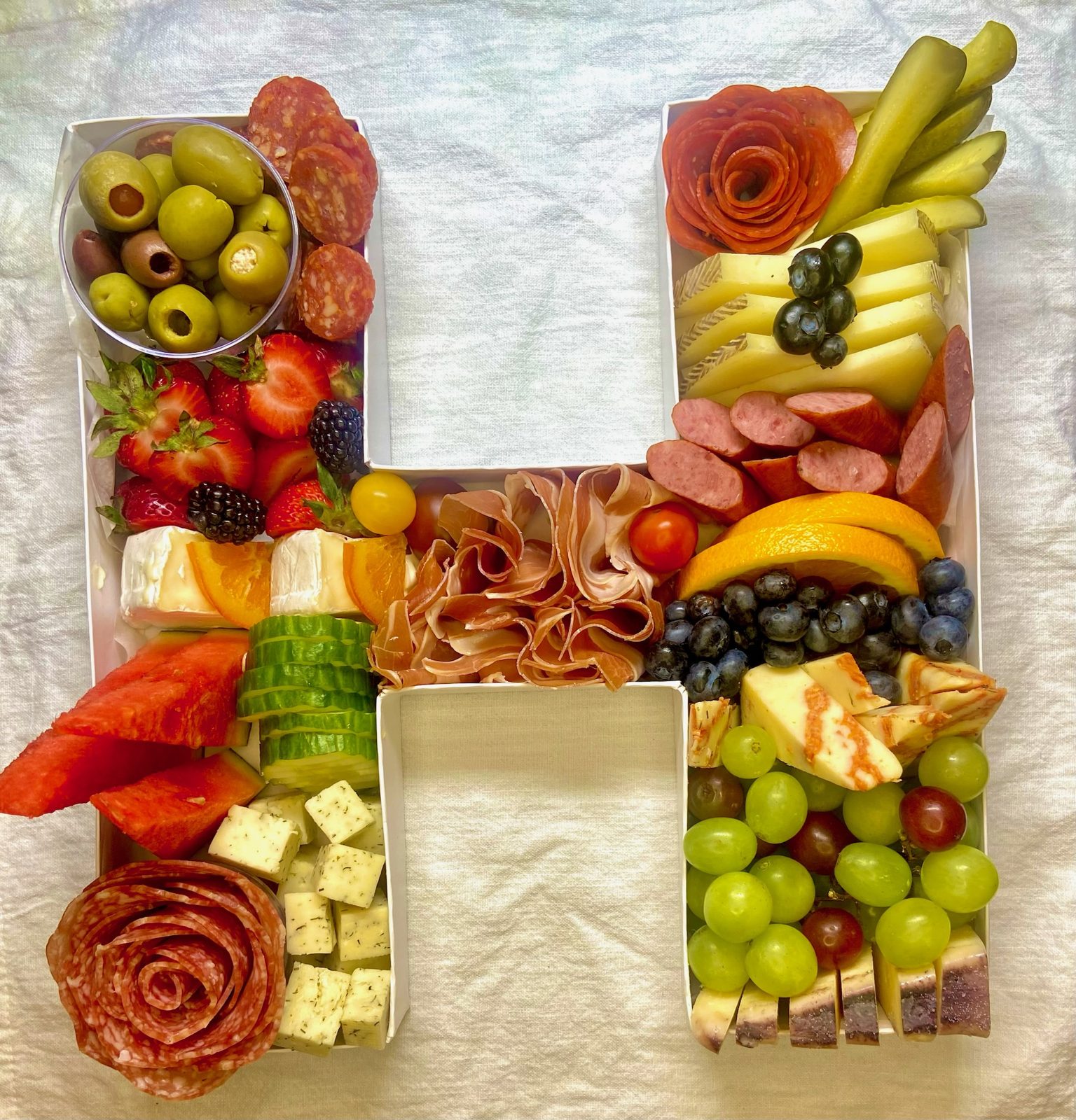 Fillable letter H filled with meats, cheeses, and fruit